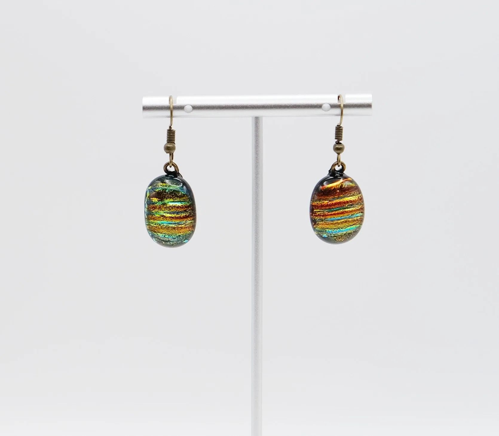 Dichroic rainbow stripes fused glass pierced dangling earrings on antiqued brass tone french wires. Approx 1.5 inches total length