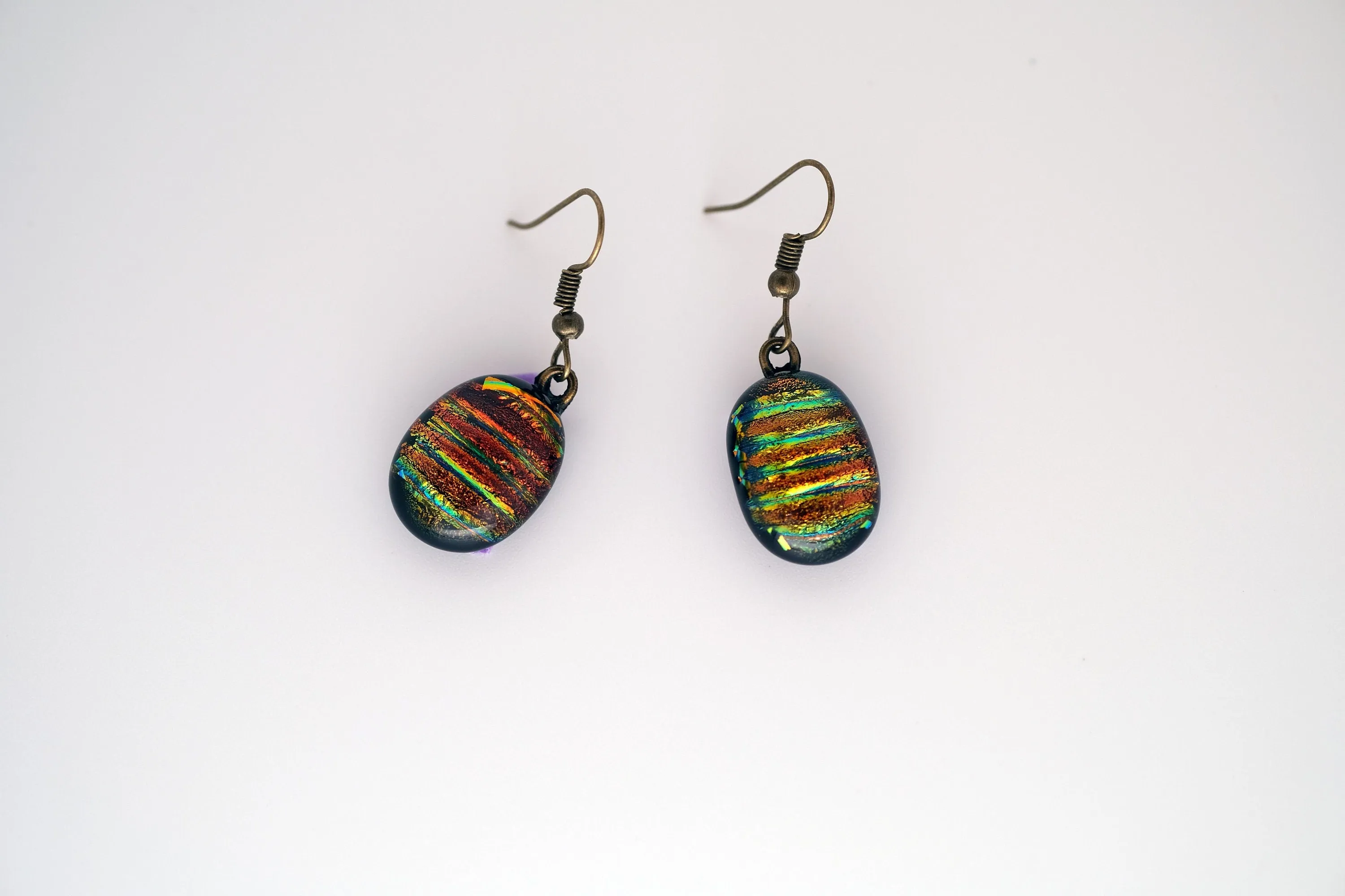 Dichroic rainbow stripes fused glass pierced dangling earrings on antiqued brass tone french wires. Approx 1.5 inches total length